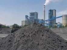 A grey, powdery fly ash mound in the foreground, with a coal-fired power plant and ash handling facility in the background.