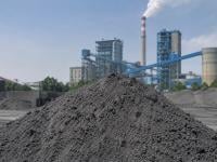 A grey, powdery fly ash mound in the foreground, with a coal-fired power plant and ash handling facility in the background.